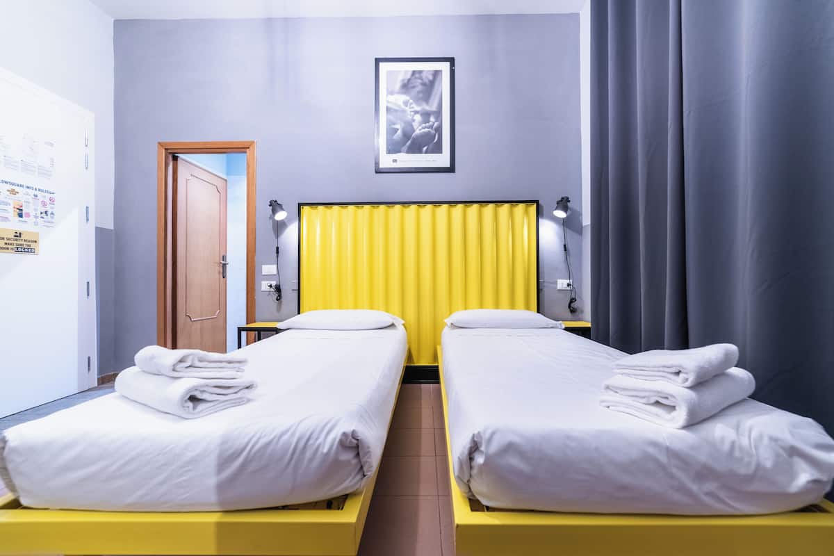 A hotel room with two beds, a yellow headboard, a framed picture on the wall, and a door to the left.