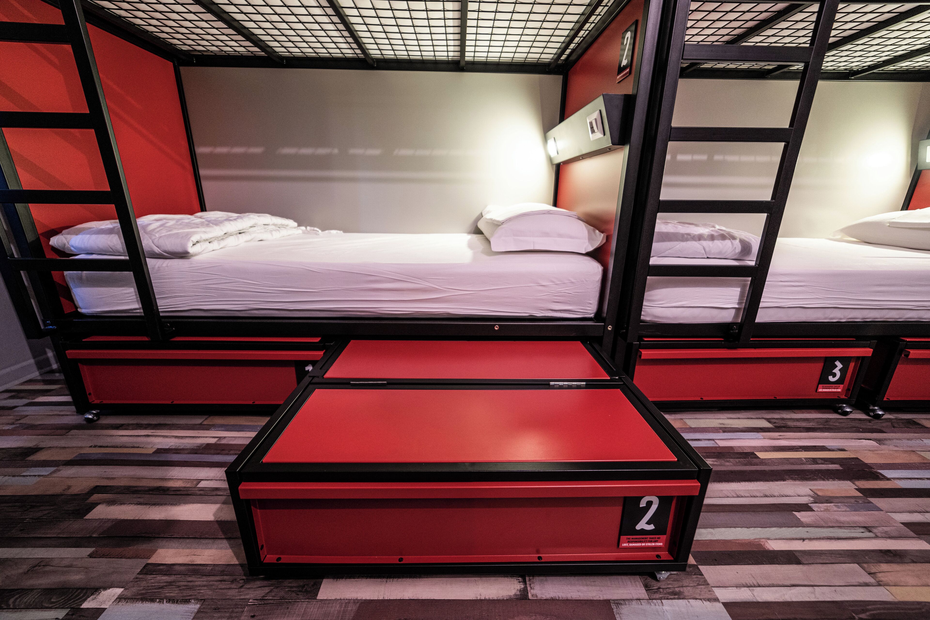 A bunk bed room with two beds, each with a red base and white bedding.
