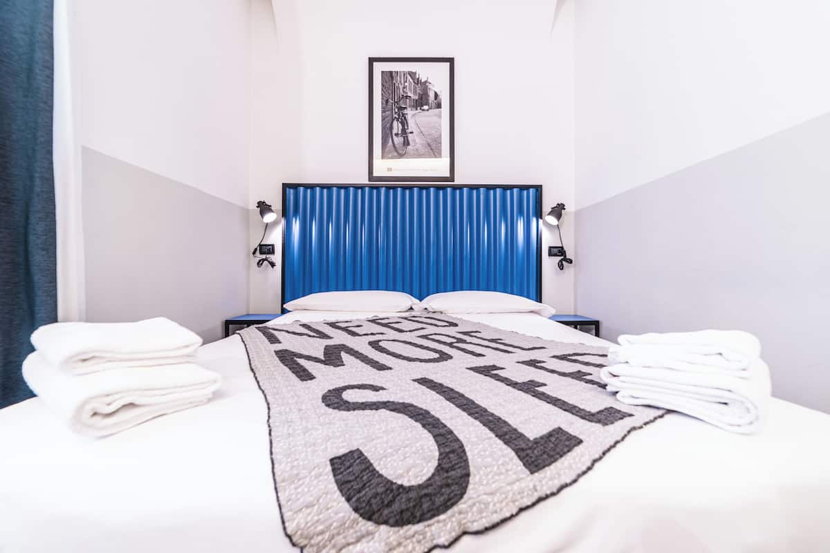 A neatly made bed with a large, bold blanket that reads "WEEKS MORE SLEEP" and a framed picture above it.