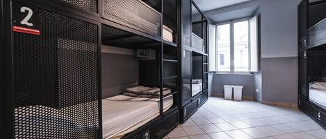 A dormitory room with bunk beds, numbered compartments, and a window providing natural light.