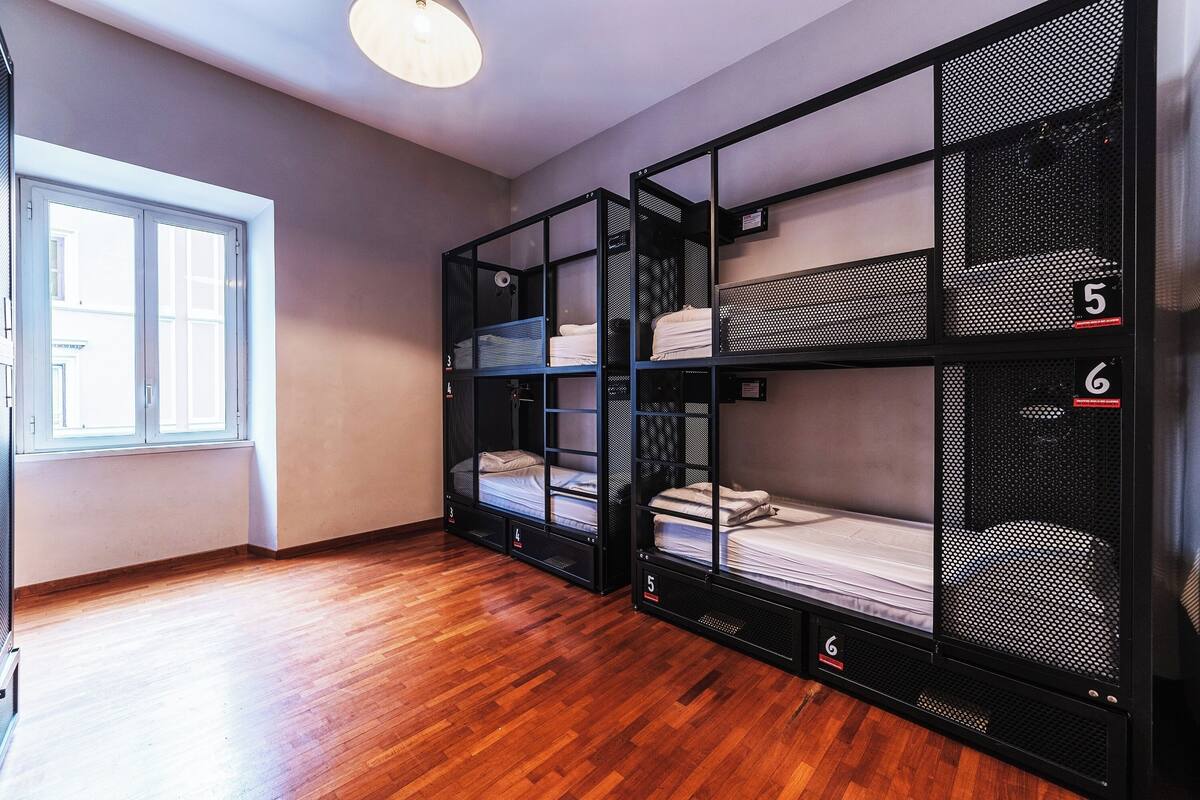 A room with two bunk beds, wooden flooring, a window, and a ceiling light.
