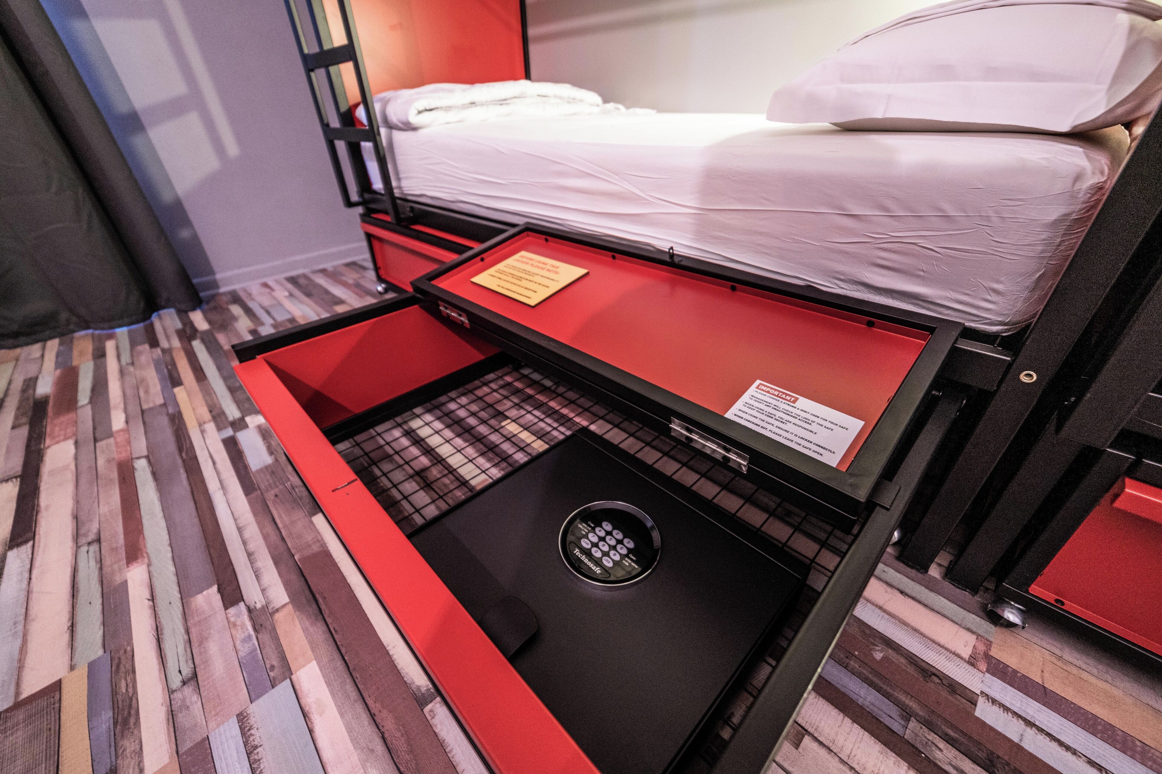 A compact room with a bunk bed, a small desk with a red tray, and a patterned floor.