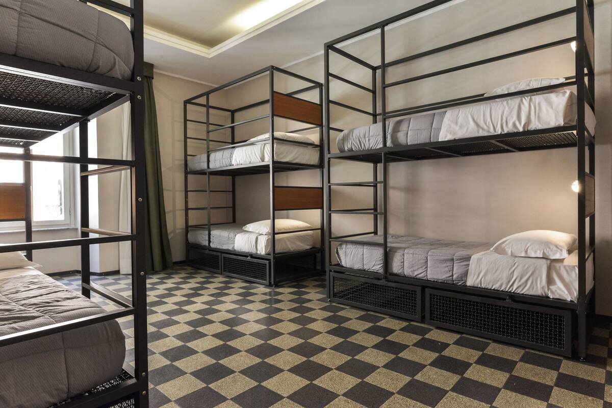 A dormitory room with bunk beds, checkered floor, and a window with curtains.