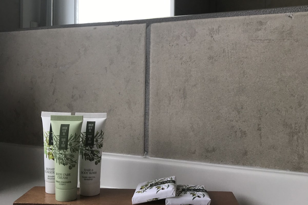 A bathroom with a bathtub, a window with blinds, and toiletries on a shelf.