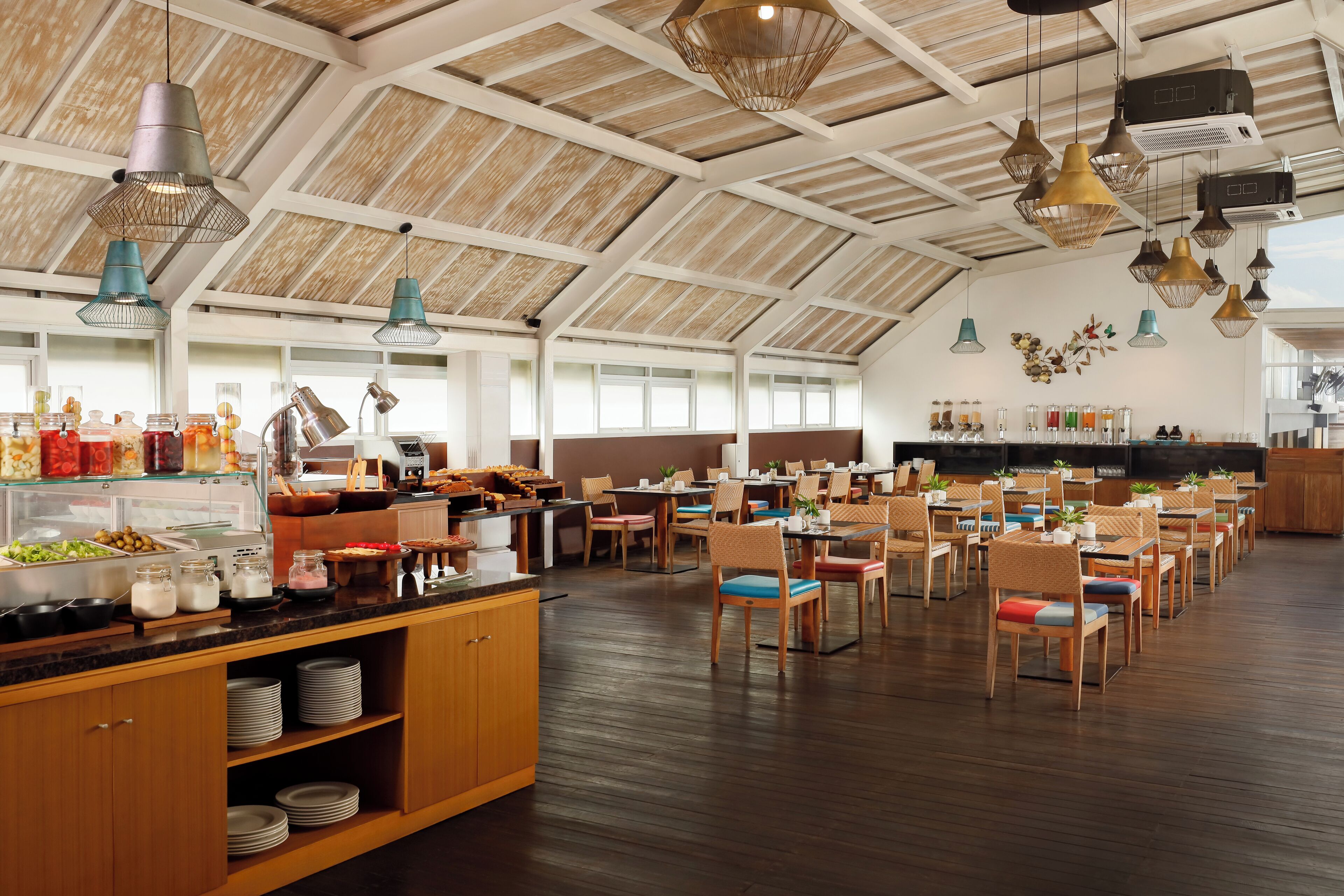 A spacious dining area with multiple tables and chairs, a buffet counter with various food items, and pendant lighting.