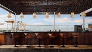 Eine Bar mit Holzwandverkleidung, hängenden Pendelleuchten und Blick zum Himmel.