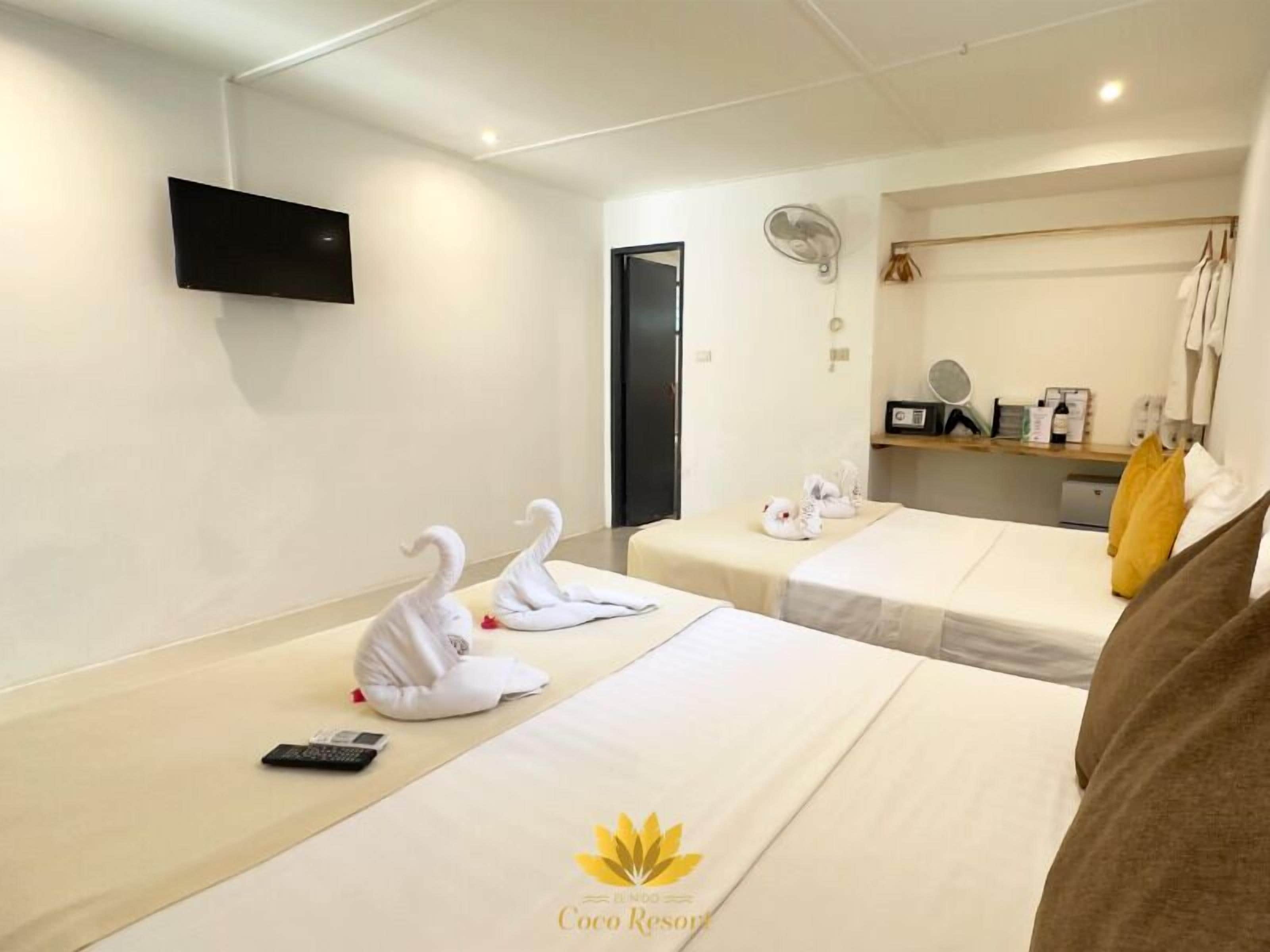 Habitación de hotel con dos camas, un televisor montado en la pared, una mesita con artículos de tocador y un espejo.