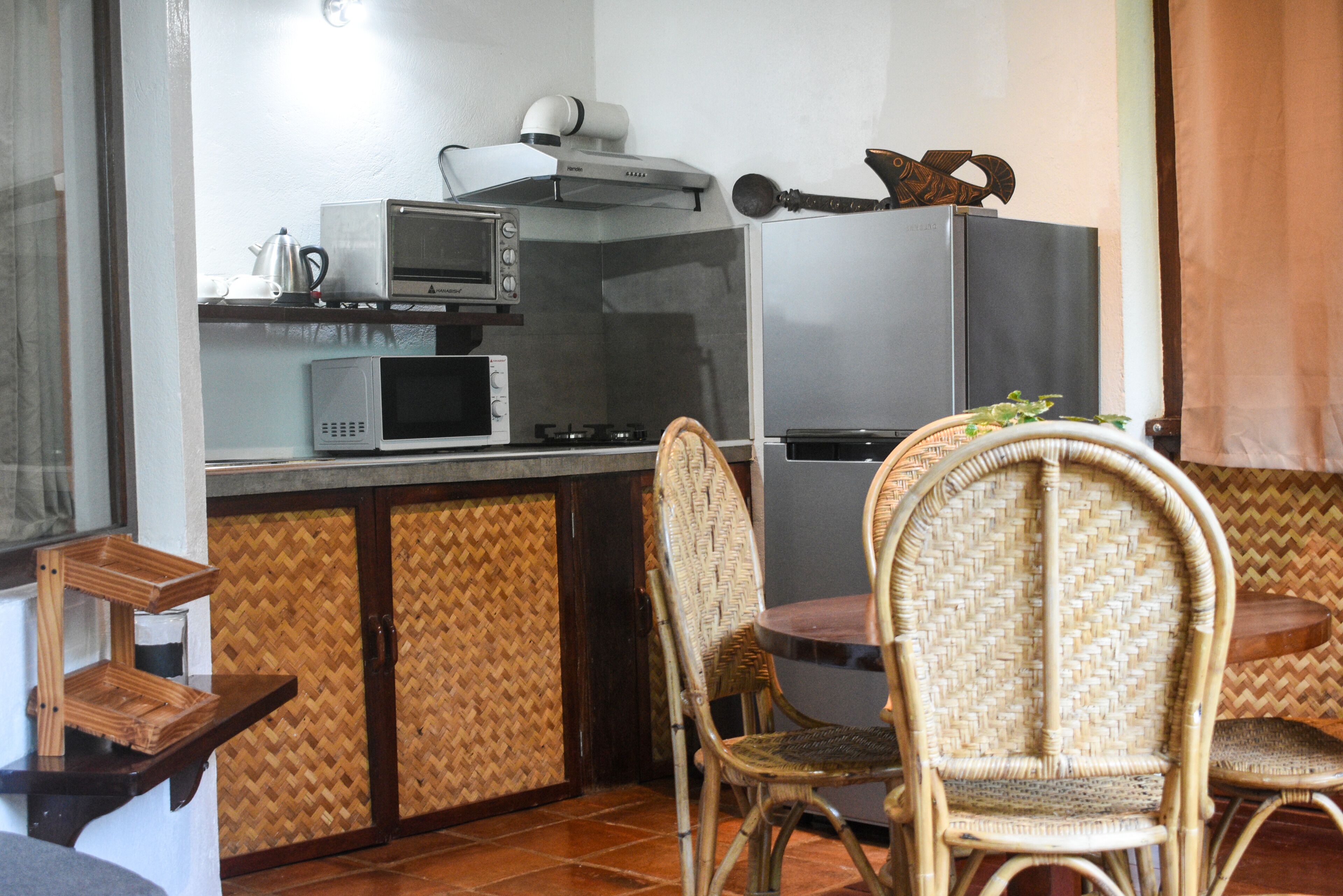 A compact kitchen with a microwave, stove, and refrigerator. There are wicker chairs around a small dining table.