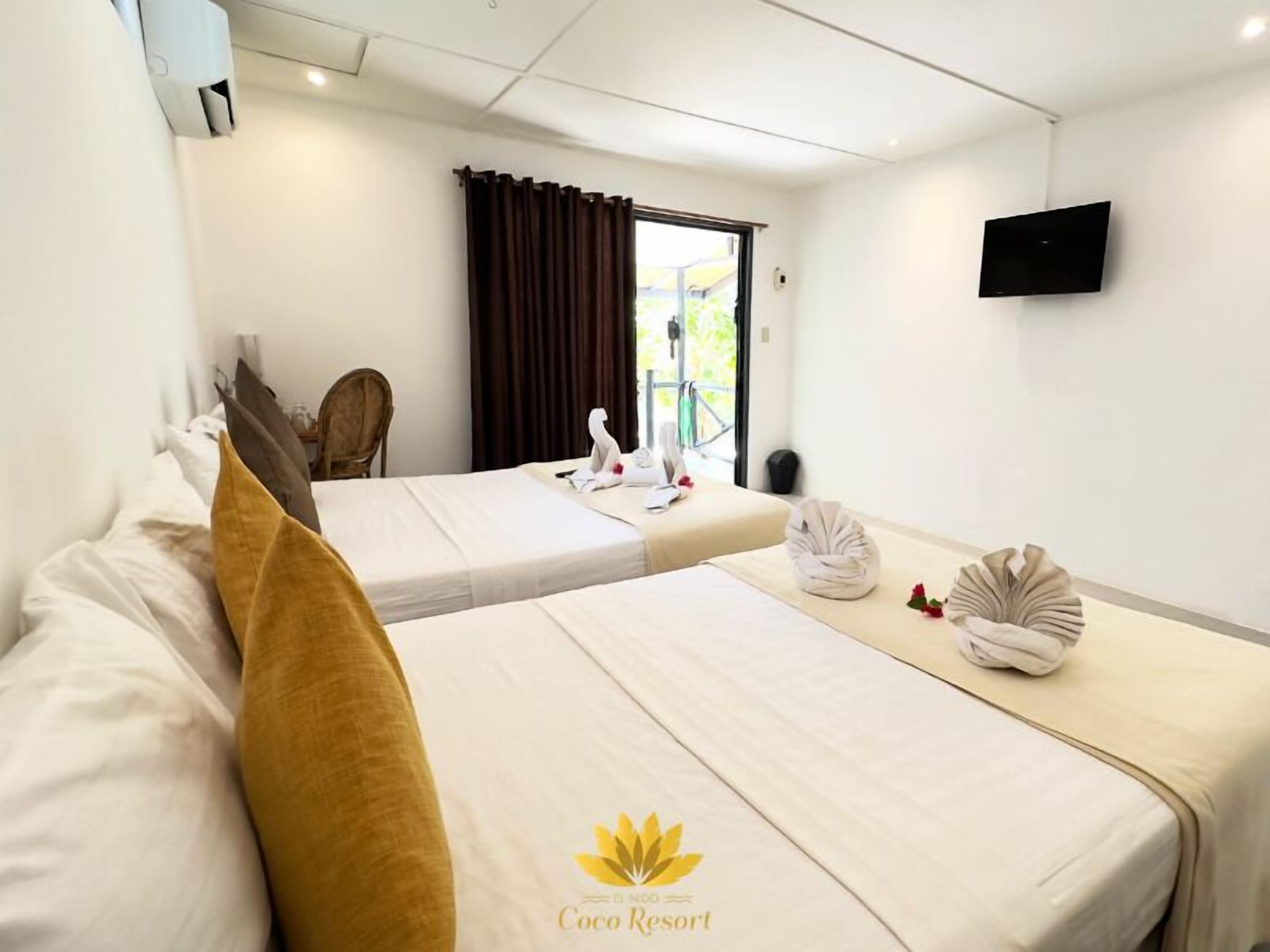 A hotel room with two beds, a TV, a window with curtains, and a swan decoration.