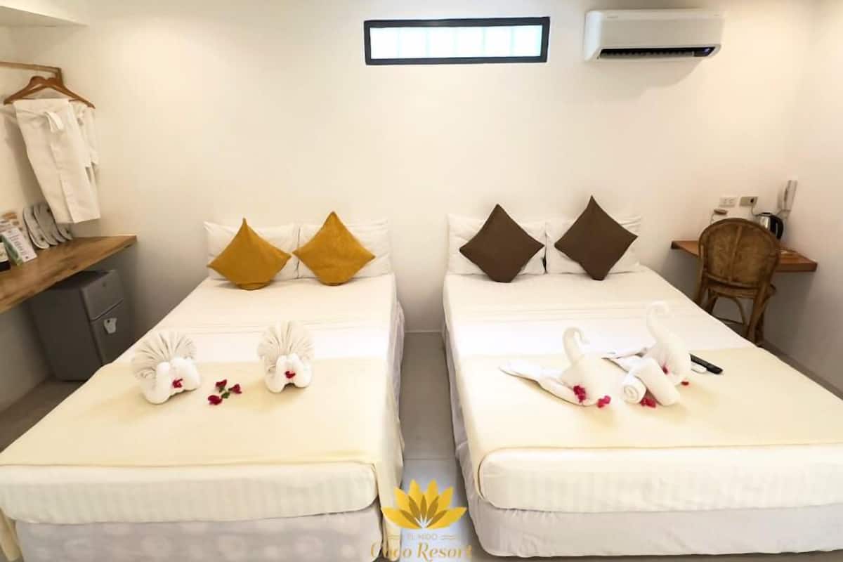 A hotel room with two beds, each with a white duvet, pillows, and decorative swans with flowers. There is a desk with a chair, a small cabinet, and an air conditioning unit on the wall.