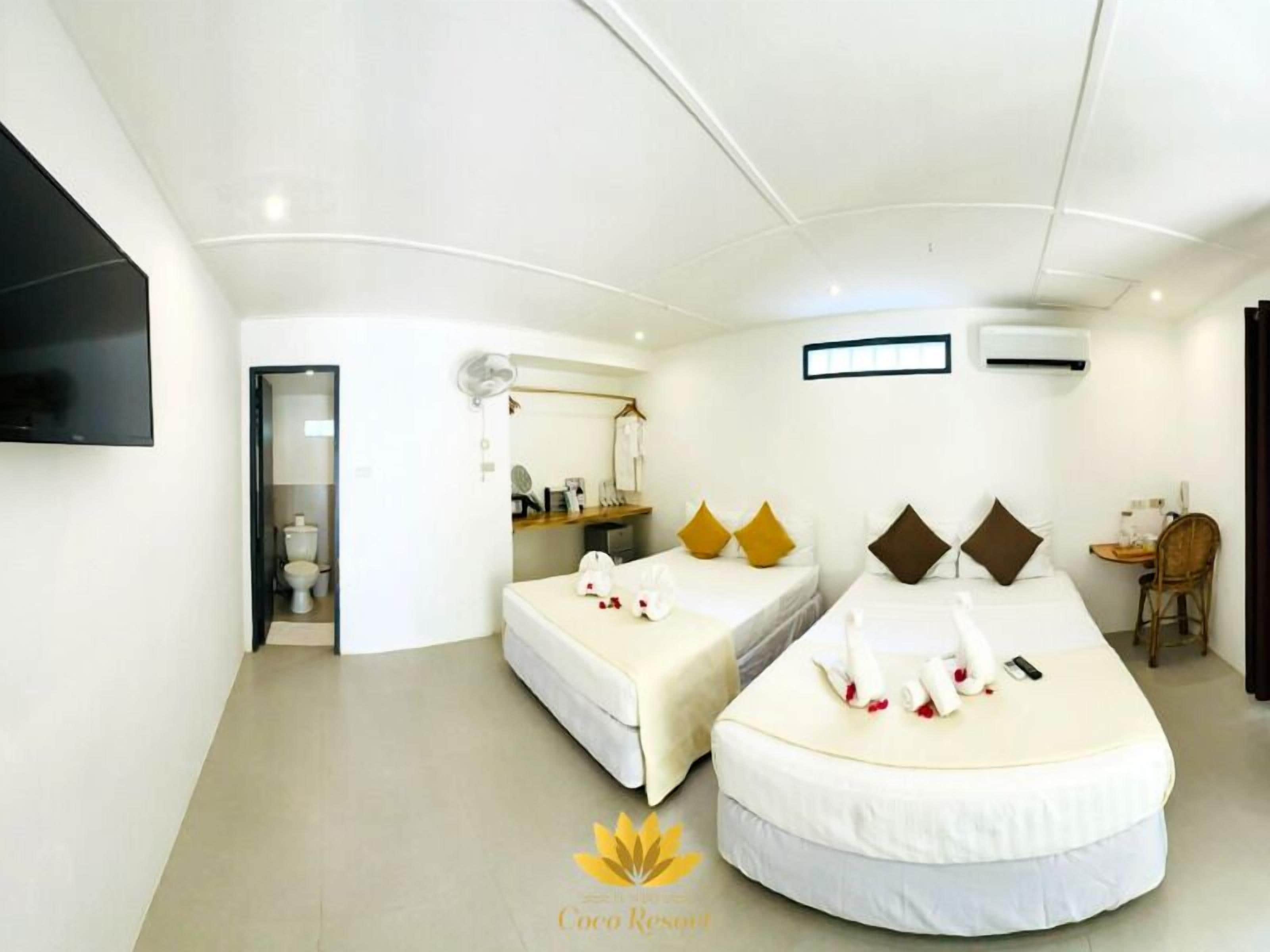 A hotel room with two beds, a TV, a desk, and an air conditioner.