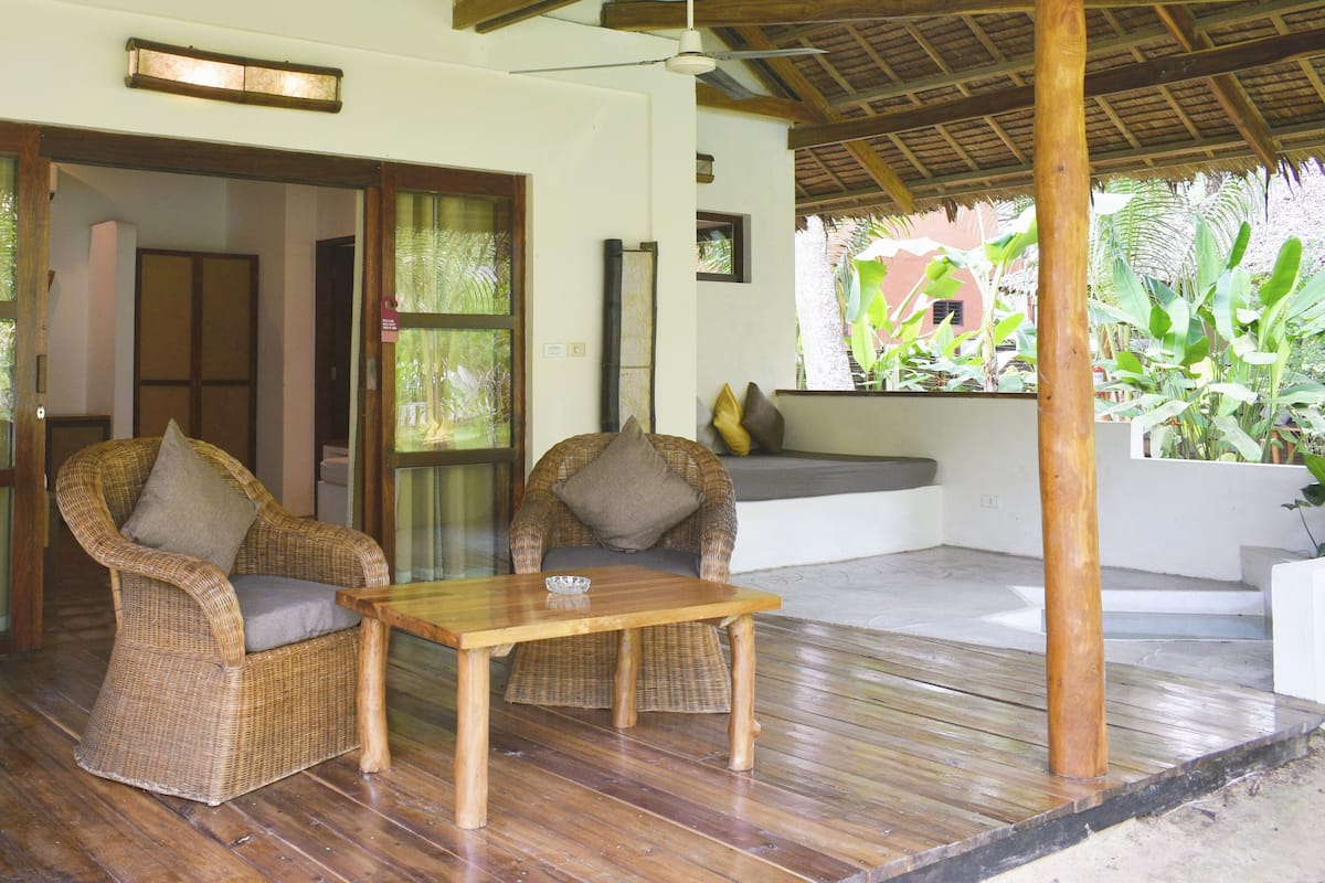 A wooden-floored room with wicker furniture and a glass door leading outside.