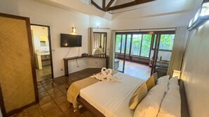 A hotel room with a large bed, a desk, a TV, and a balcony with a view of greenery. - El Nido Coco Resort (El Nido)