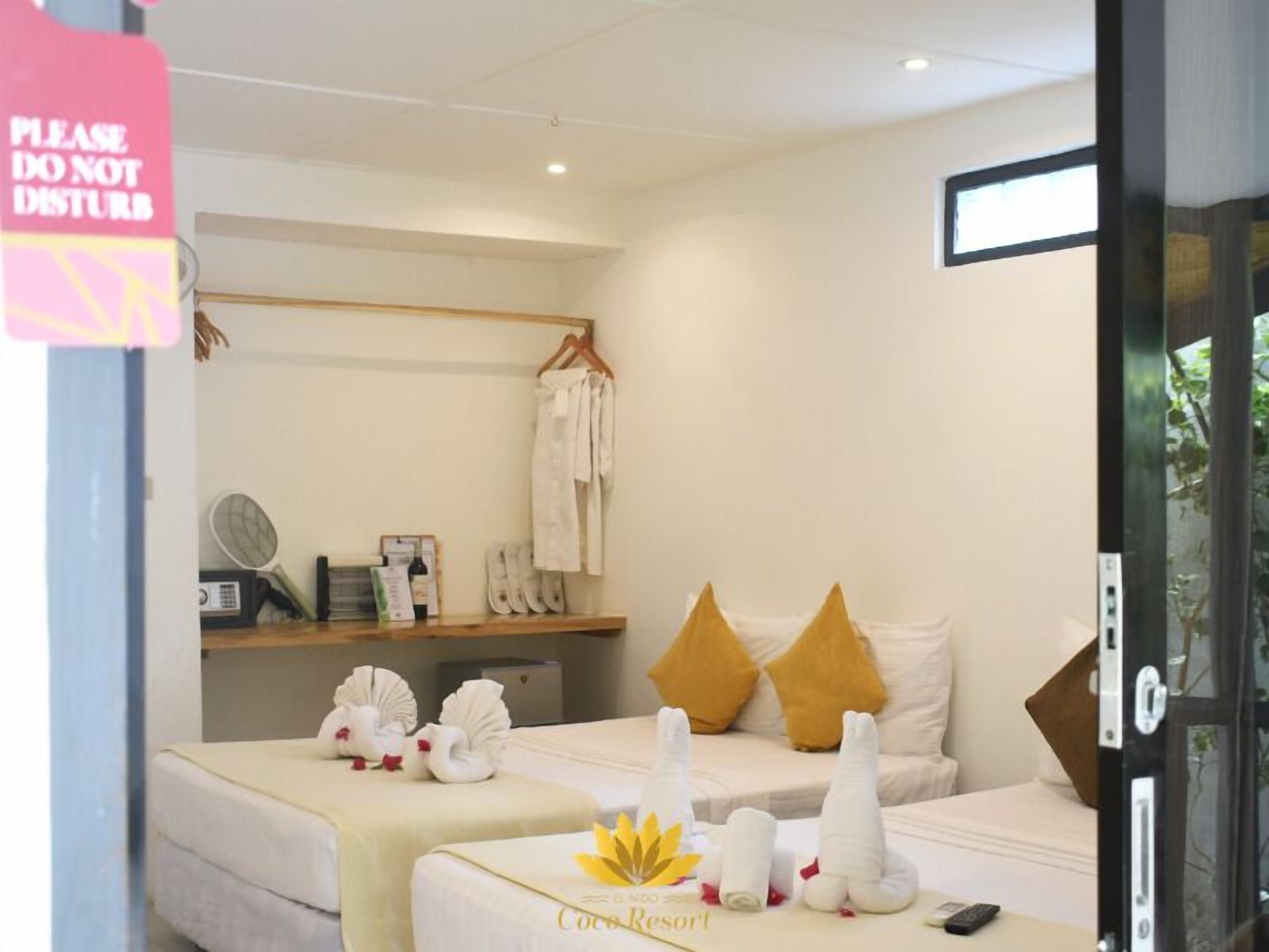 A hotel room with two beds, a shelf with towels and toiletries, a sign that says "PLEASE DO NOT DISTURB", and a view of the outdoors through a glass door.