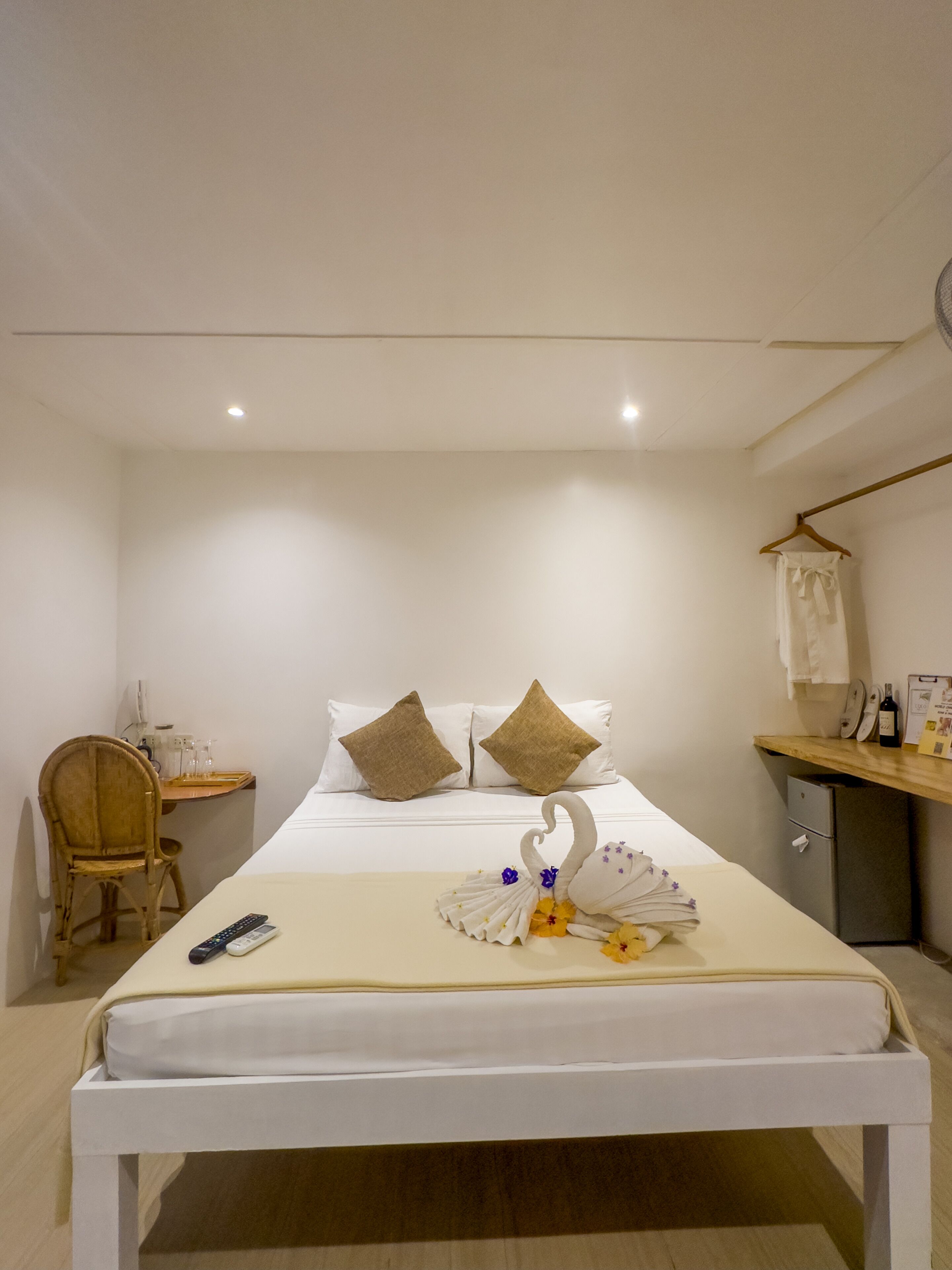A neatly arranged hotel room with a bed, a bedside table, a chair, and a small desk with a computer and a wine bottle.