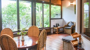 A room with a wooden dining table, wicker chairs, a cushioned bench, and a small wooden table with a lamp. - El Nido Coco Resort (El Nido)