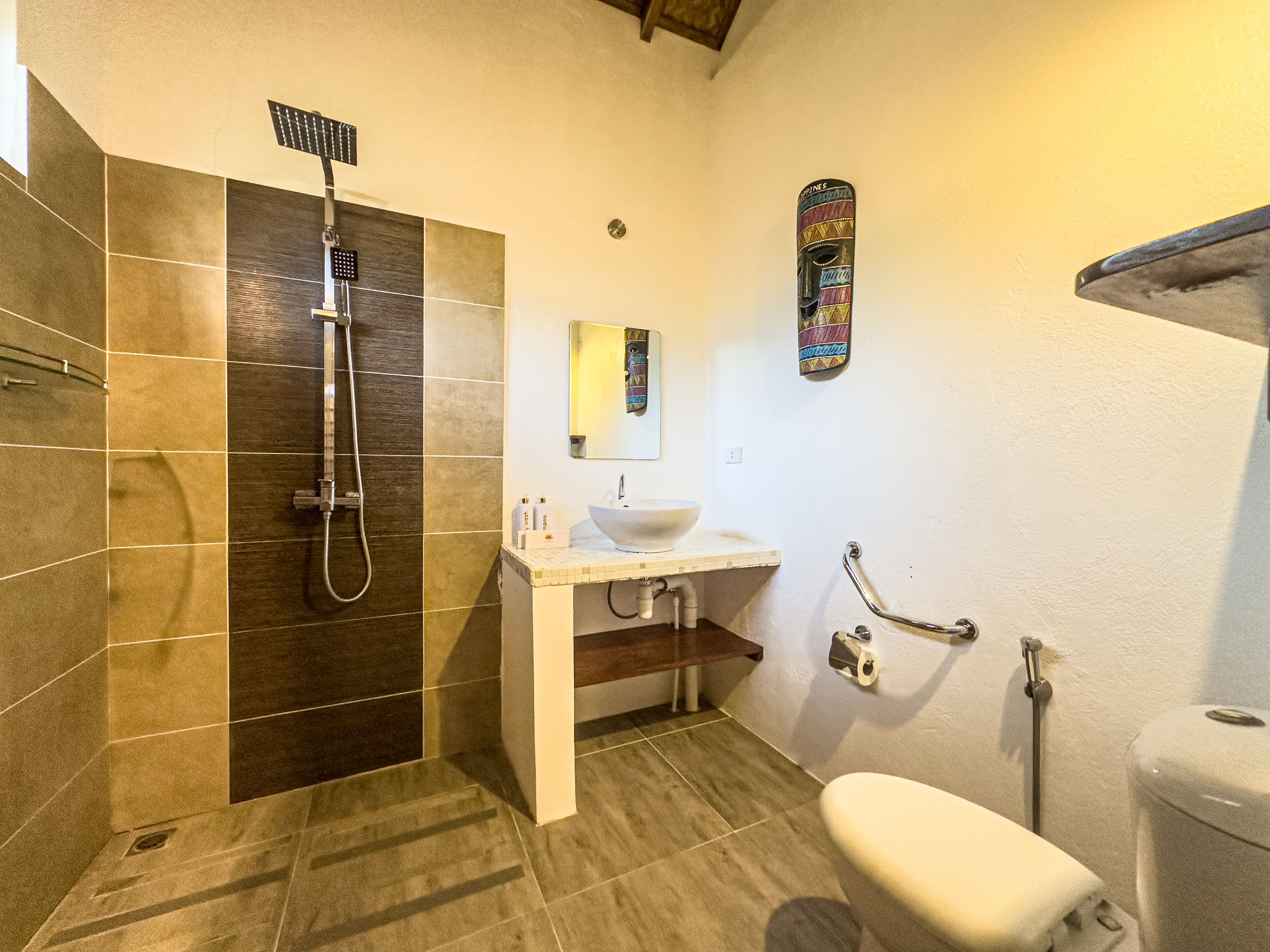 A bathroom with a shower, sink, toilet, and a decorative mask on the wall.