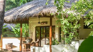 A thatched-roof structure with a wooden porch, wicker furniture, and a view of the surrounding greenery. - El Nido Coco Resort (El Nido)