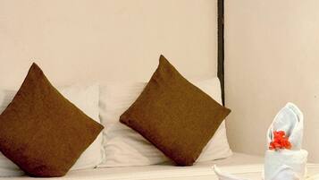 Una cama bien hecha con dos almohadas marrones, una blanca y una toalla blanca con un detalle floral rojo.