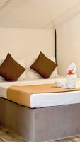 Una cama bien hecha con dos almohadas marrones, una blanca y una toalla blanca con un detalle floral rojo.