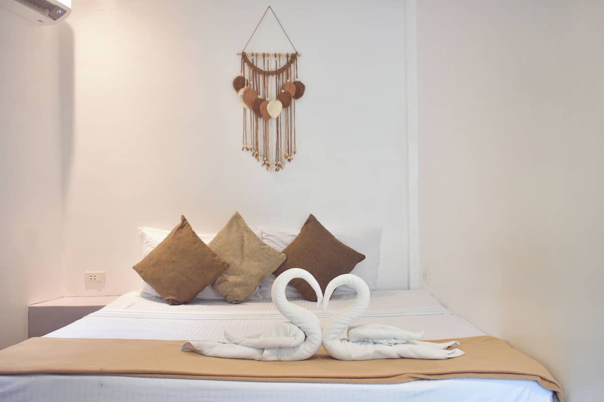 A neatly made bed with a heart-shaped towel arrangement, a wall-mounted macrame decoration, and two brown pillows.