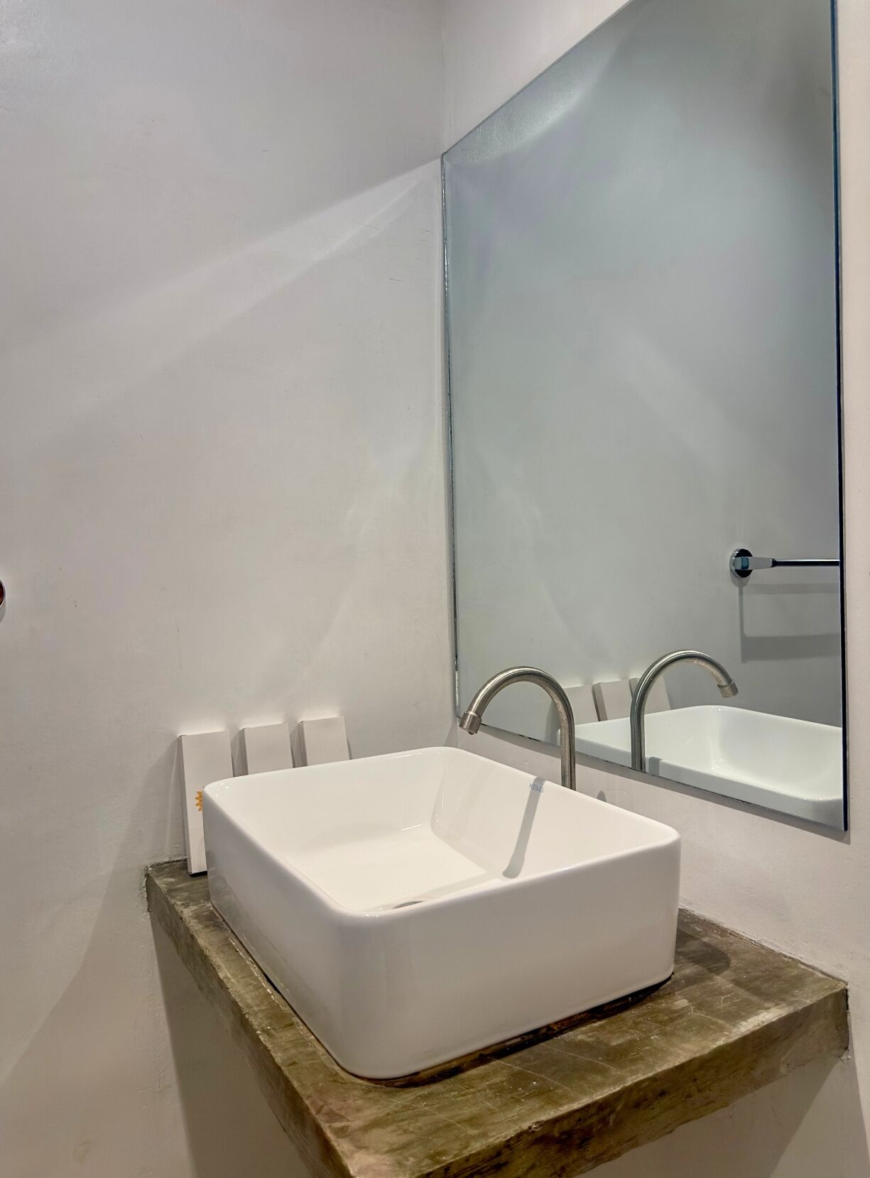 A bathroom with a white rectangular sink, a modern faucet, and a large mirror above it.
