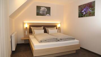A bedroom with a bed, bedside lamps, a radiator, and two framed pictures on the wall.