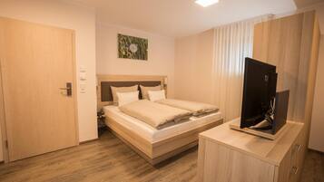A bedroom with a wooden bed, a TV on a wooden cabinet, and a door.