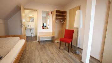 A hotel room with a bed, a red chair, a bench, a wardrobe, a mirror, and a lamp.
