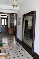 Un pasillo con suelo de baldosas, un banco de madera, un espejo grande y una puerta que da a otra habitación.