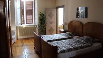 Ein Schlafzimmer mit zwei Holzbett, einem Heizkörper, einem Fenster mit Jalousien, einer Tür und einer Pflanze.