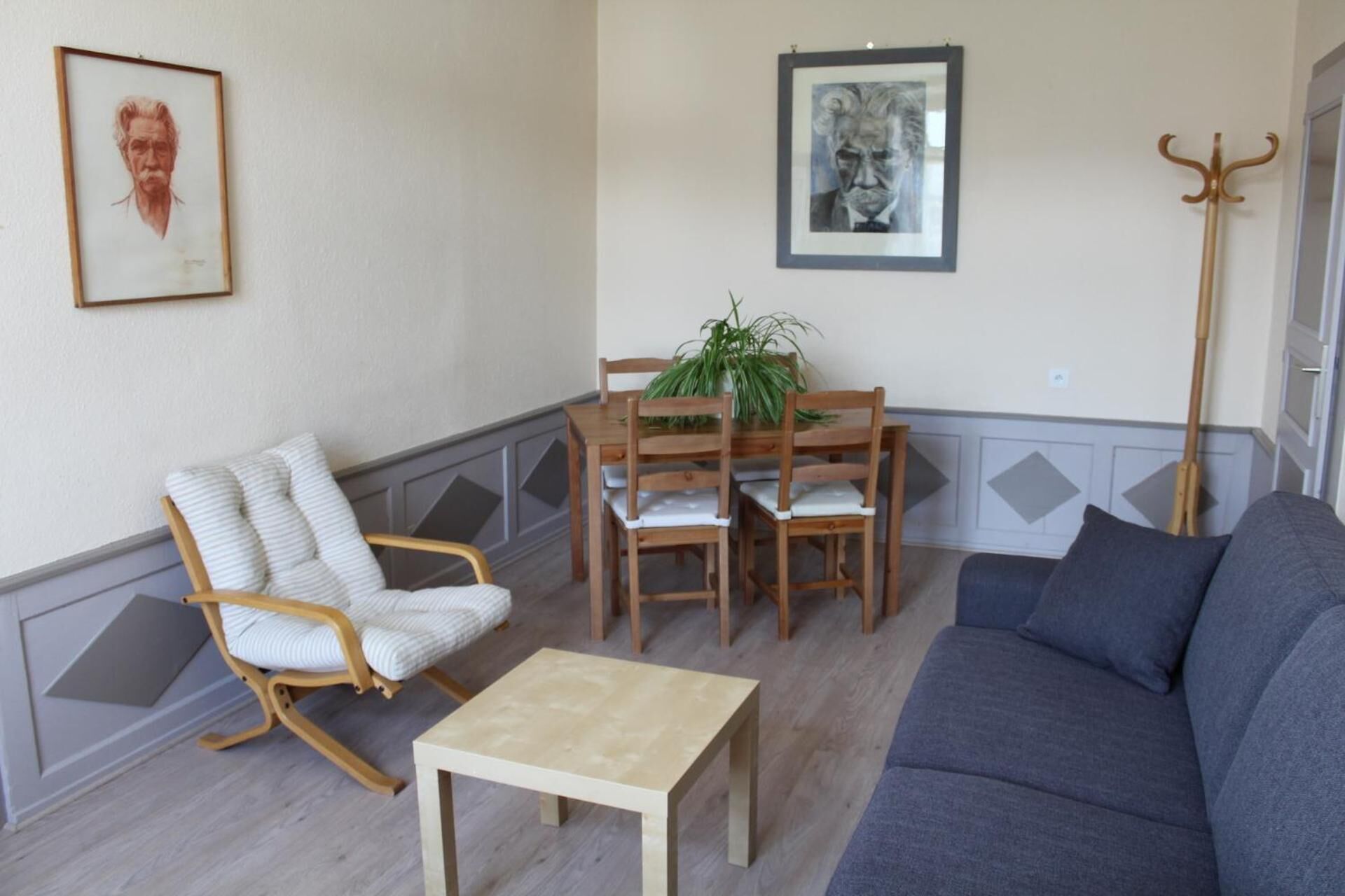 Un salon comprenant un canapé, une table à manger en bois avec des chaises, un fauteuil à rayures et deux œuvres d’art encadrées accrochées au mur.