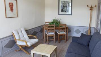 Un salon comprenant un canapé, une table à manger en bois avec des chaises, un fauteuil à rayures et deux œuvres d’art encadrées accrochées au mur.