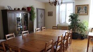 A dining room with a wooden table and chairs, a bookshelf, and a chandelier. - Ancien Presbytère Albert Schweitzer (Gunsbach)