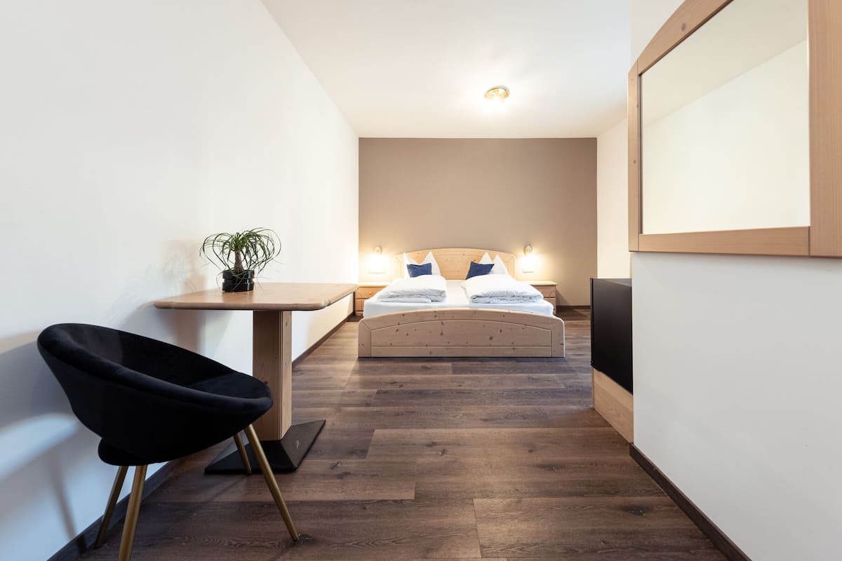 A narrow hotel room with a bed, bedside tables, a small desk, and a chair.