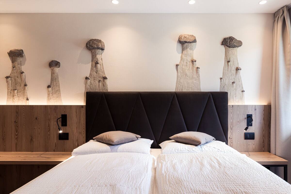 A modern bedroom with two beds, a wooden headboard, and wall-mounted light fixtures.