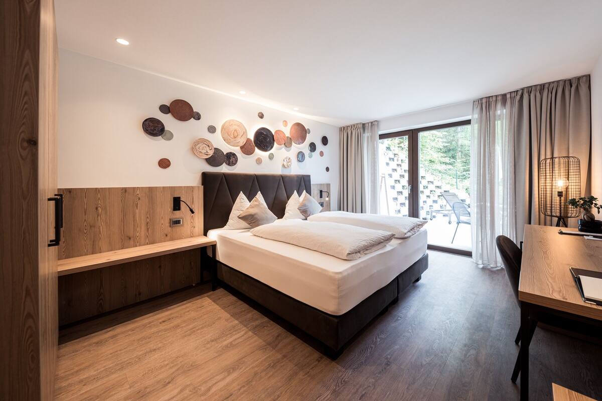 A modern hotel room with a large bed, a wooden bench, a desk, and a wall decorated with circular art pieces.