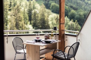 A balcony with a table set for two, a bottle of wine, and a scenic view of a forested valley. - Hotel Berghang (Cornedo All'isarco)