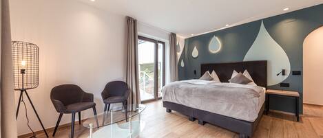 Un dormitorio moderno con una cama grande, dos sillones, una mesa de vidrio y una lámpara de pie.