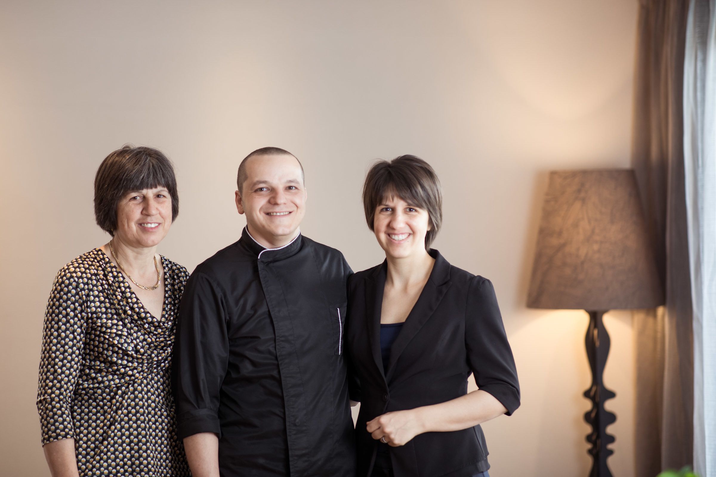 Three people standing in a room with a lamp in the background.