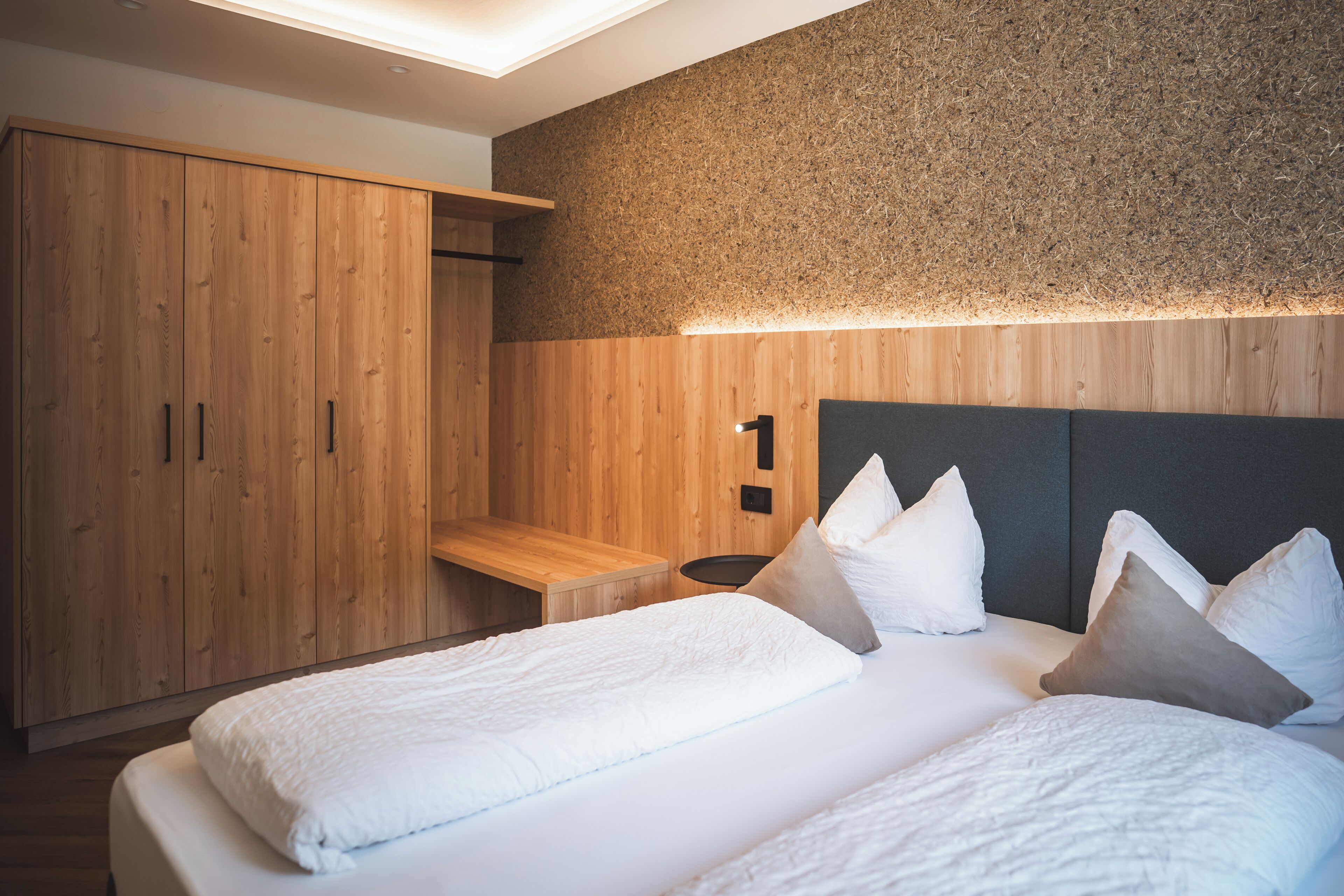 A bedroom with a bed, pillows, a wooden wardrobe, and a textured wall.