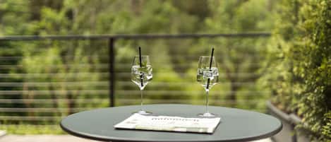 A round table with two glasses of water and a menu on a balcony with a view of greenery.