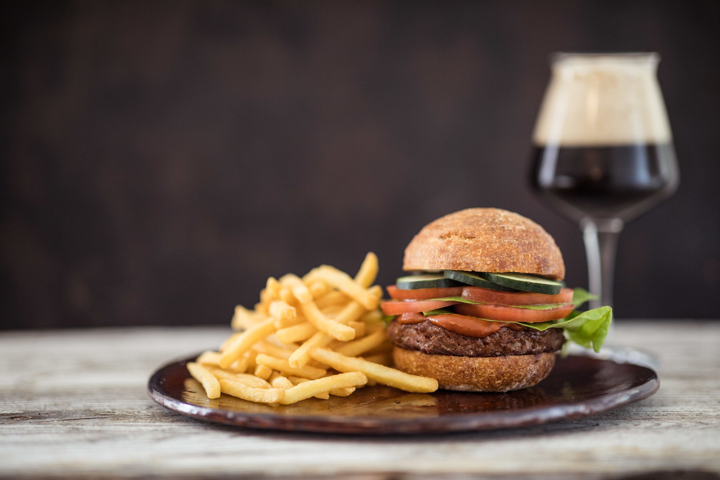 A burger with fries and a glass of red wine on a wooden table.