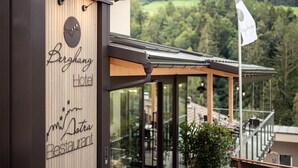 Exterior moderno de un hotel con fachada de madera, un letrero de restaurante y vistas a un paisaje boscoso.