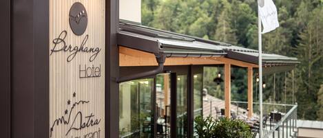 A modern hotel exterior with a wooden facade, a restaurant sign, and a view of a forested landscape.
