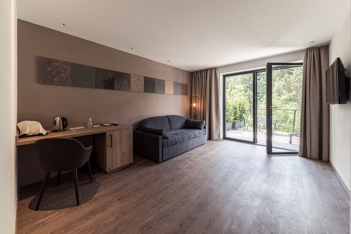 A modern room with a wooden desk, a dark sofa, and a sliding glass door leading to an outdoor area.