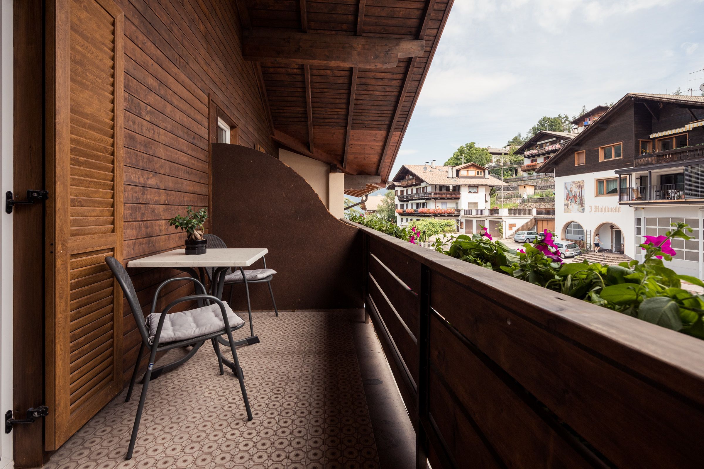 Ein Balkon mit Holzgeländer, einem Tisch und zwei Stühlen.