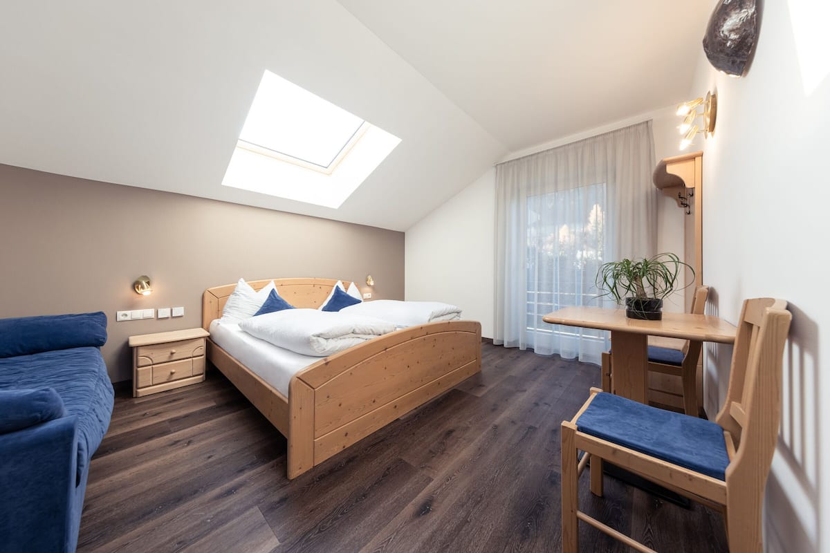 A bedroom with a skylight, a bed, a desk, a chair, and a potted plant.