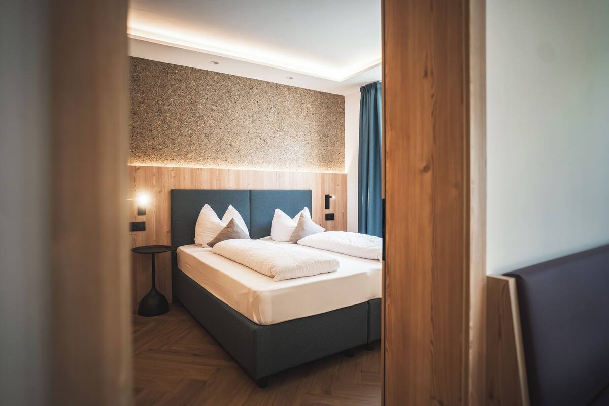 A modern hotel room with a bed, bedside tables, and a textured wall.