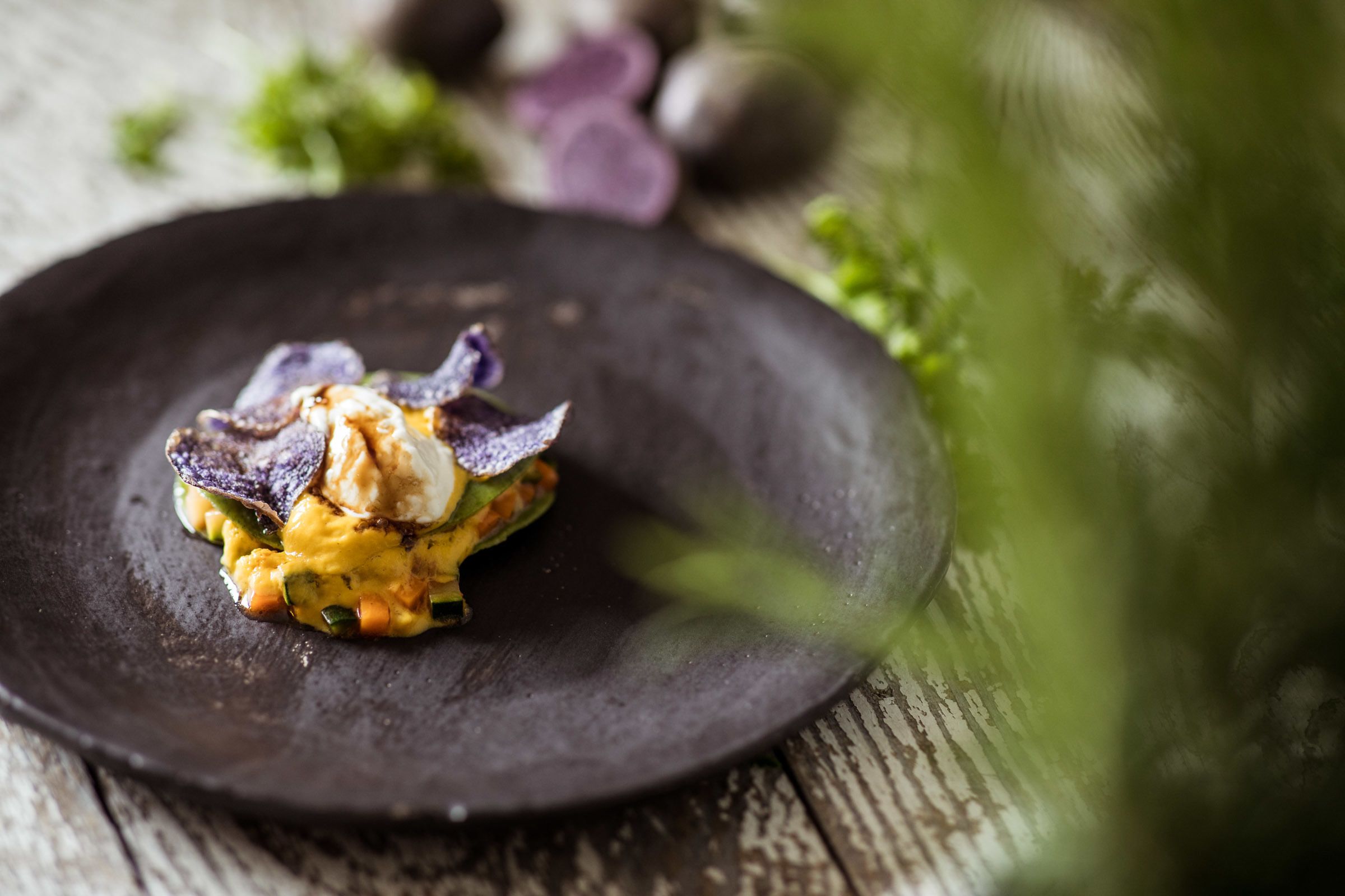 Un plato oscuro con un alimento, posiblemente una ensalada o aperitivo, sobre una mesa de madera rústica.